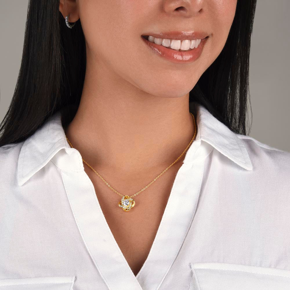 Gold love knot pendant necklace worn by smiling woman — delicate gold chain with crystal knot pendant, graduation gift for daughter, women's jewelry